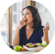 A woman enjoying grapes with a variety of fruits and a fresh salad.
